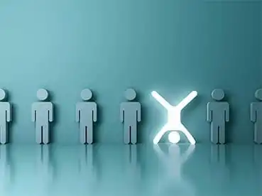 A row of five minimalist humanoid figures made from identical shapes. Four figures are standing upright, depicted in blue-grey. The middle figure is glowing white and is positioned upside down, standing on its head with legs in the air.